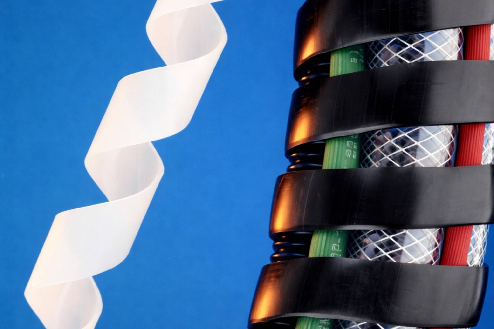 Blue background with a twisting white ribbon on the left and a black segmented cylindrical object with colored insides on the right.